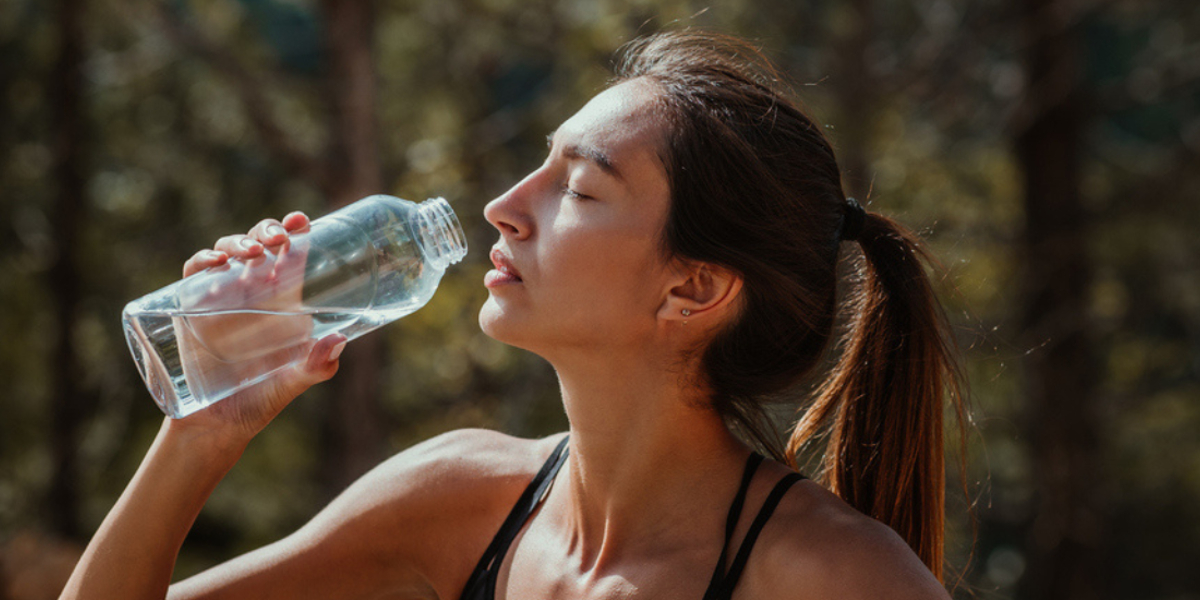 foto van vrouw die uit een glazen fles elektrolyten drinkt na het sporten