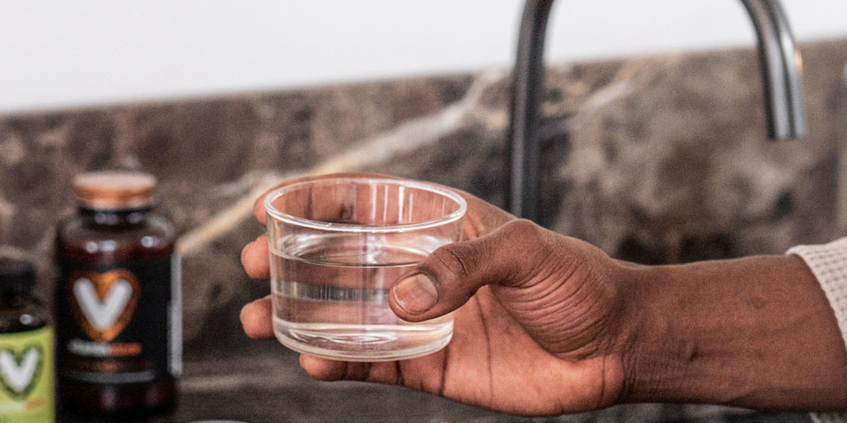 foto van hand met glas water en vitaminen op de achtergrond