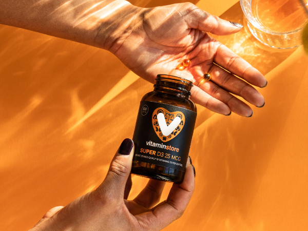vitamine d supplement met kleine capsules in een hand op een oranje achtergrond