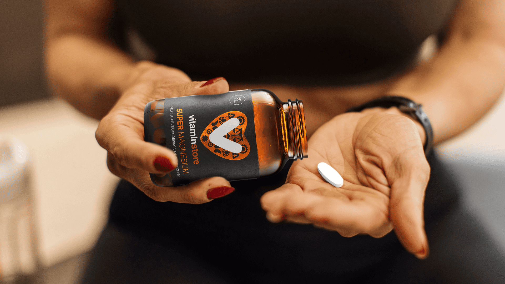 vrouwelijke handen houden een vitaminepotje vast waar een pil uit komt
